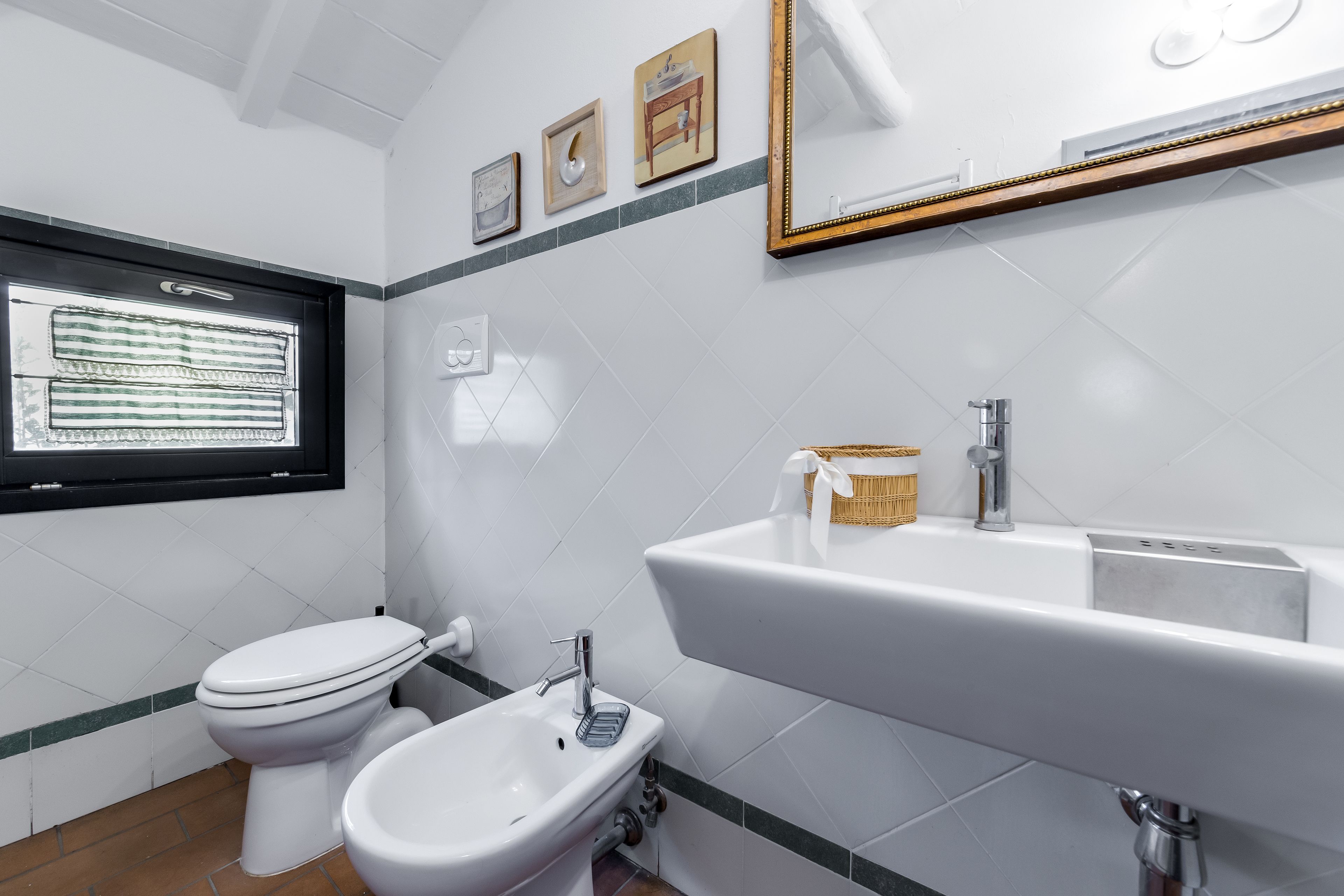 Ein Badezimmer mit Toilette, Bidet und Waschbecken. An der Wand hängen drei Bilder in Rahmen.