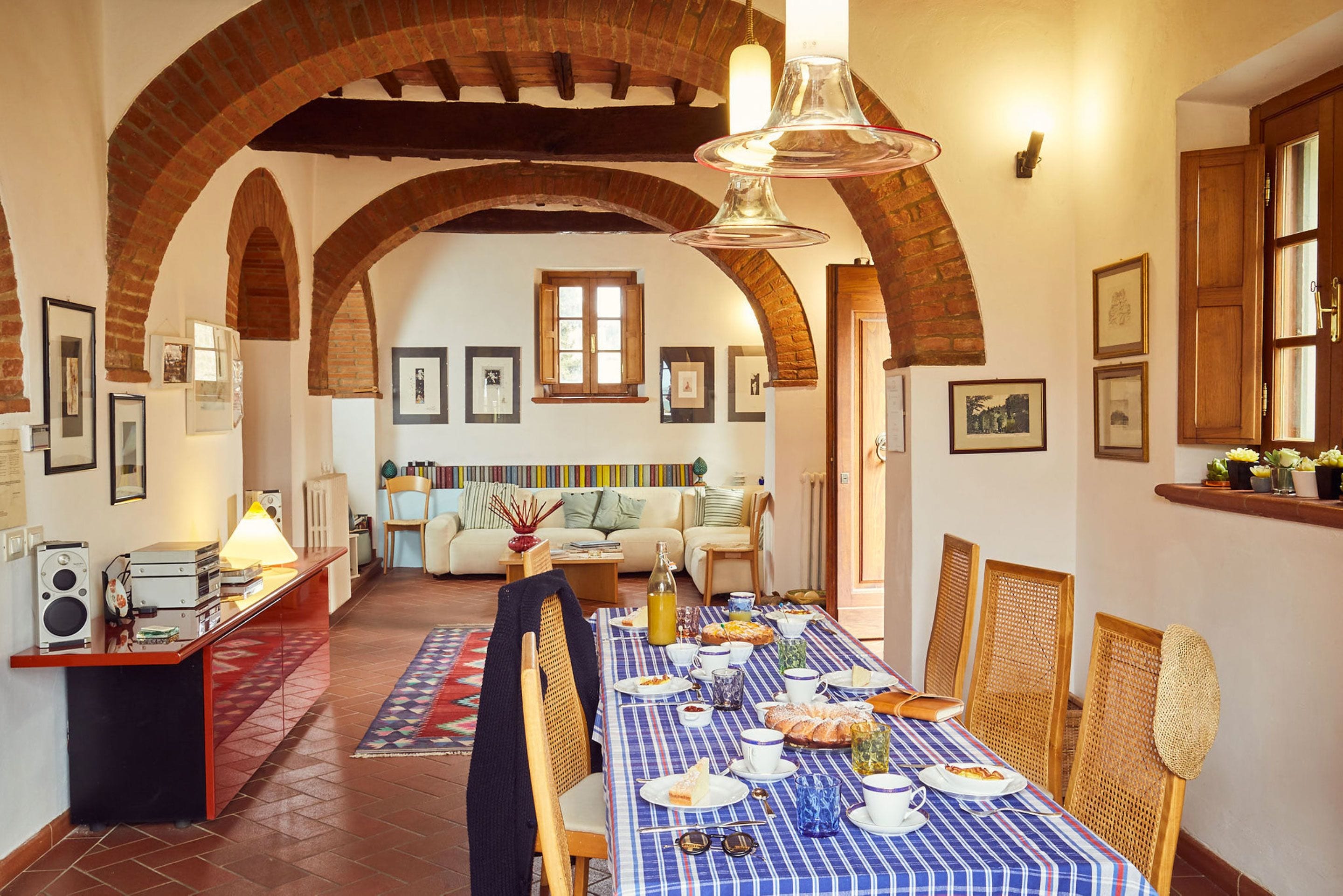 A dining area with a long table set for a meal, a sofa in the background, and a brick archway.