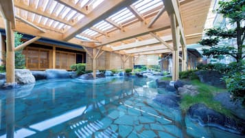 An indoor hot spring area with wooden beams, a stone-tiled floor, and a view of traditional buildings.