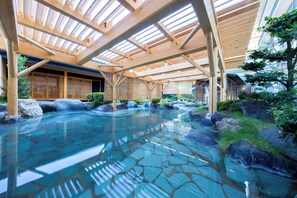 Un área de aguas termales interiores con vigas de madera, suelo de baldosas de piedra y vistas a edificios tradicionales.