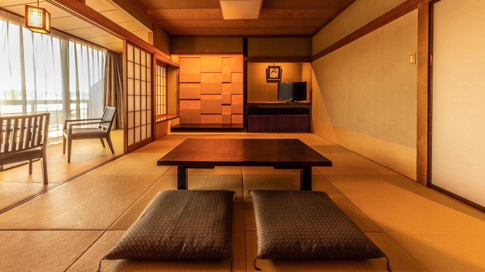 Una habitación japonesa tradicional con suelo de tatami, una mesa baja, bancos, puertas correderas y un televisor.