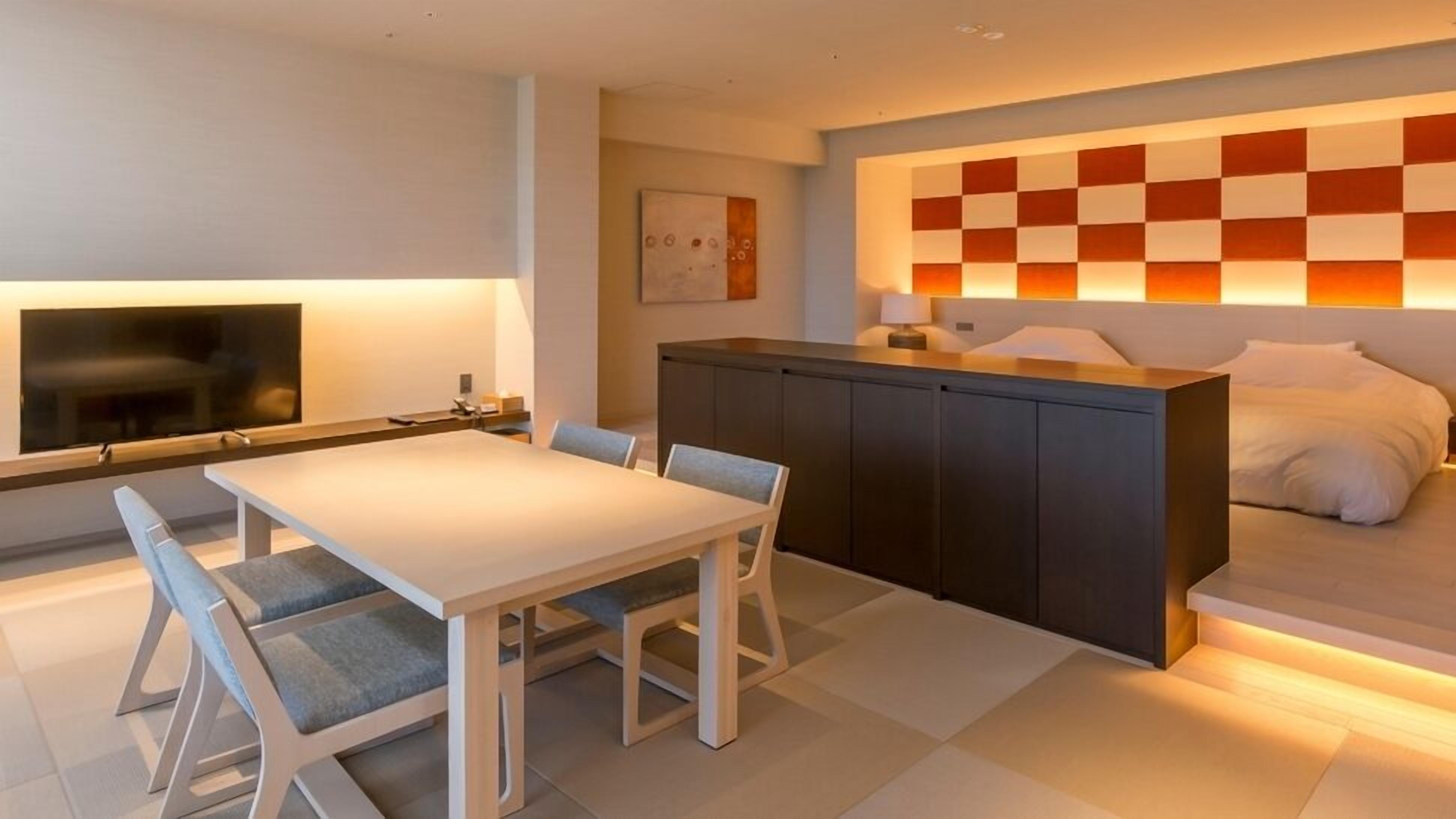 Una habitación de hotel moderna con zona de comedor, televisor, pared estampada en cuadros y cama.