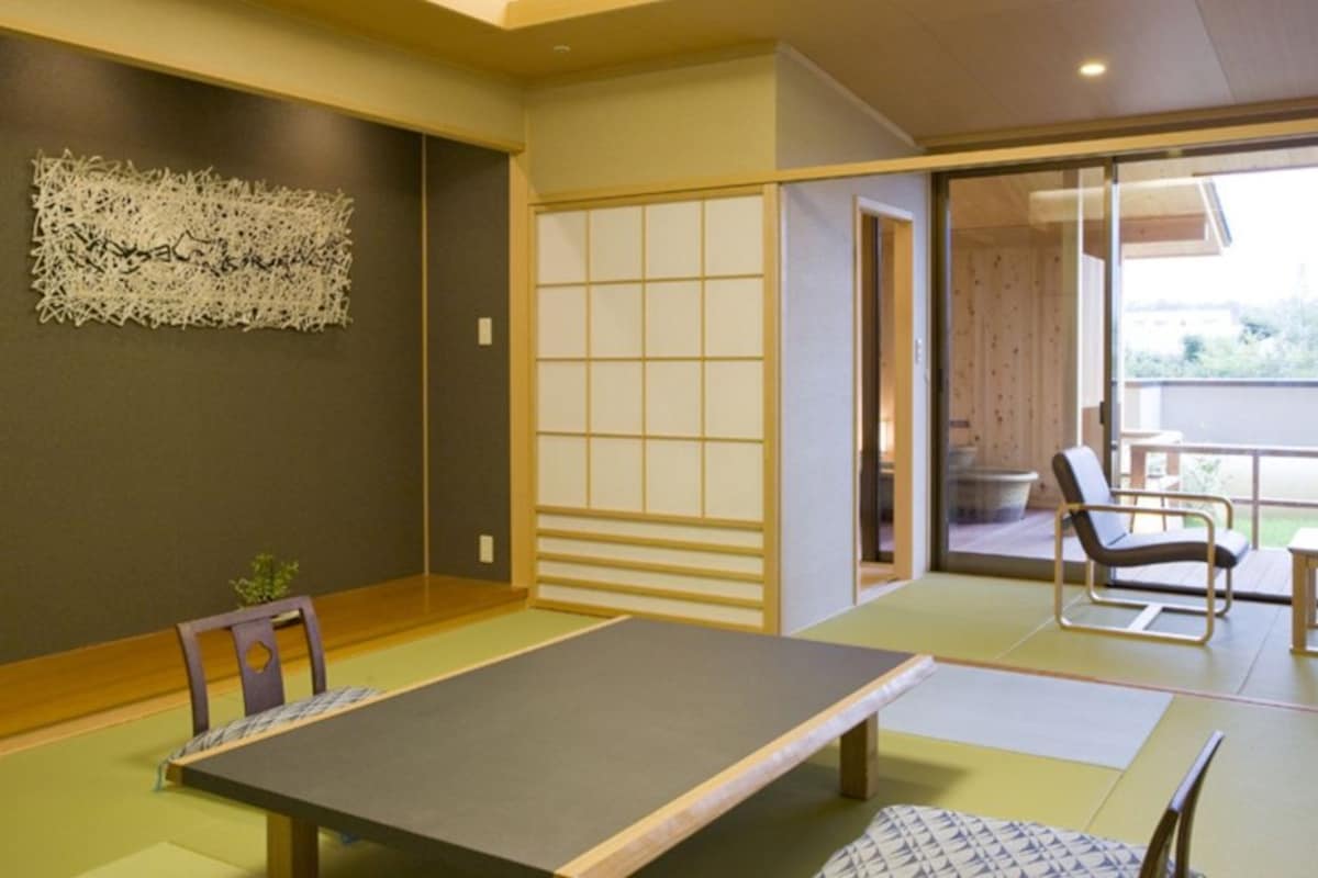 A tatami mat room with a low table and chairs, a sliding door, and a view of the outdoors.