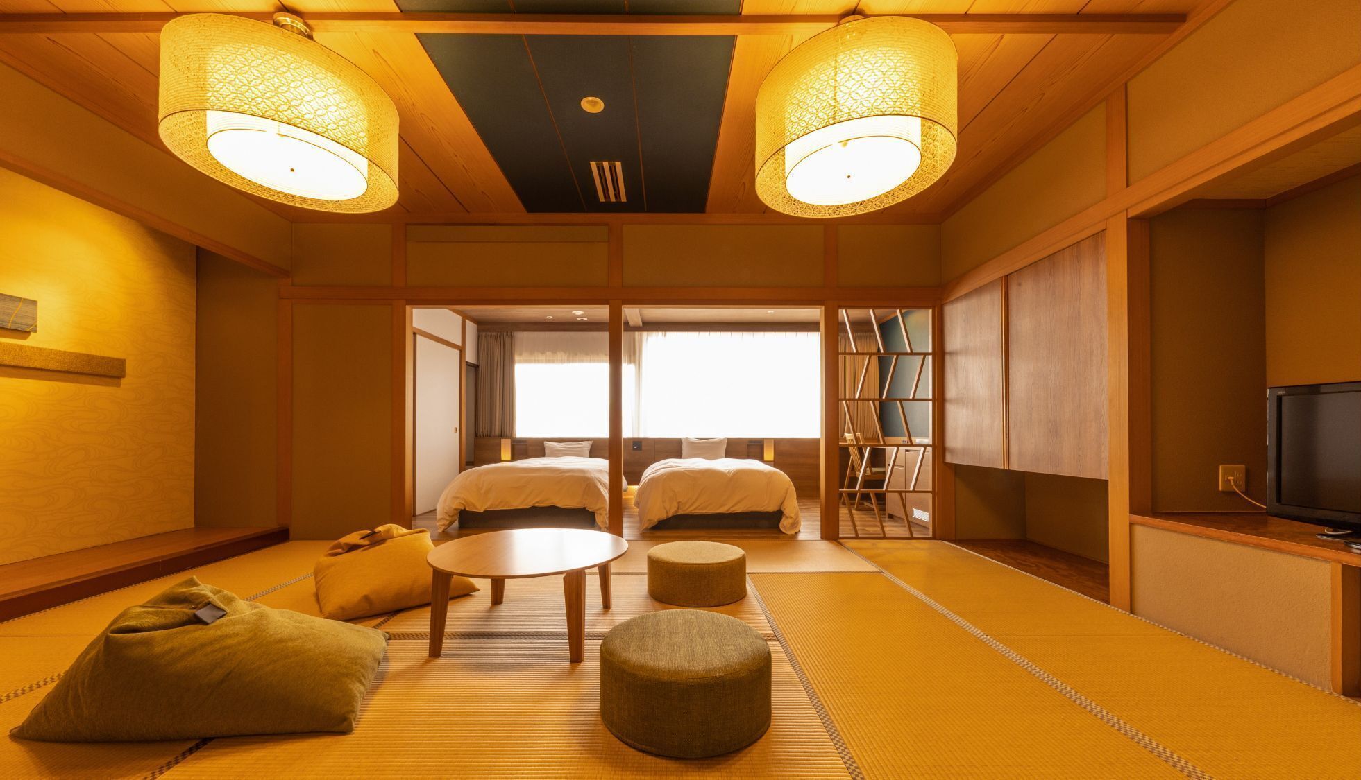 Habitació japonesa tradicional amb fons de tatami, dos llits, una taula rodona petita i una televisió.