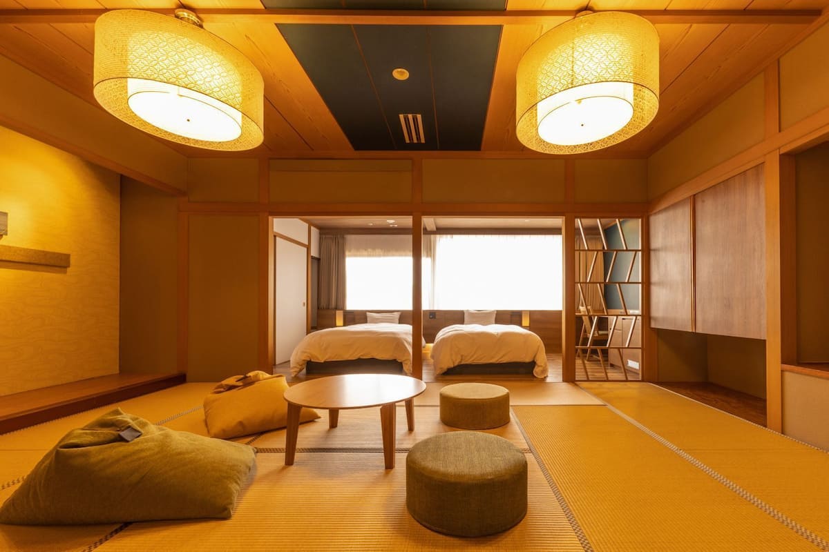 A traditional Japanese-style room with tatami flooring, two beds, a small round table, and a television.
