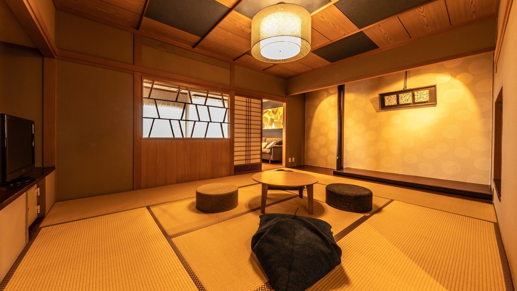 Una habitación japonesa tradicional con suelo de tatami, una mesa baja, cojines, un televisor y un biombio shoji.
