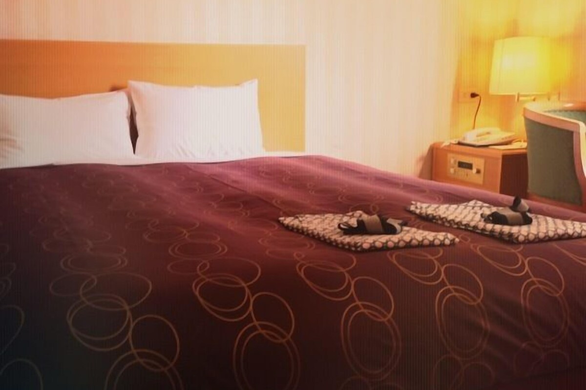 A hotel room with a large bed, a nightstand with a lamp, and a chair.