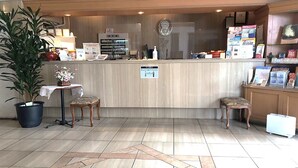 A reception area with a wooden counter, a potted plant, two stools, a clock, and a display of magazines and brochures. - Nagoya Grand Hotel (Nagoya)