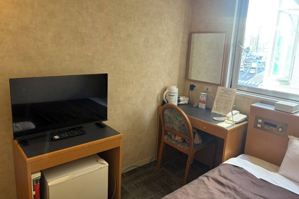 A hotel room with a bed, a desk with a computer, a chair, a television, and a window with a city view.