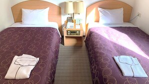 Une chambre d’hôtel avec deux lits, chacun doté d’une tête de lit, d’une table de chevet avec un téléphone et une lampe, et d’une paire de serviettes pliées.