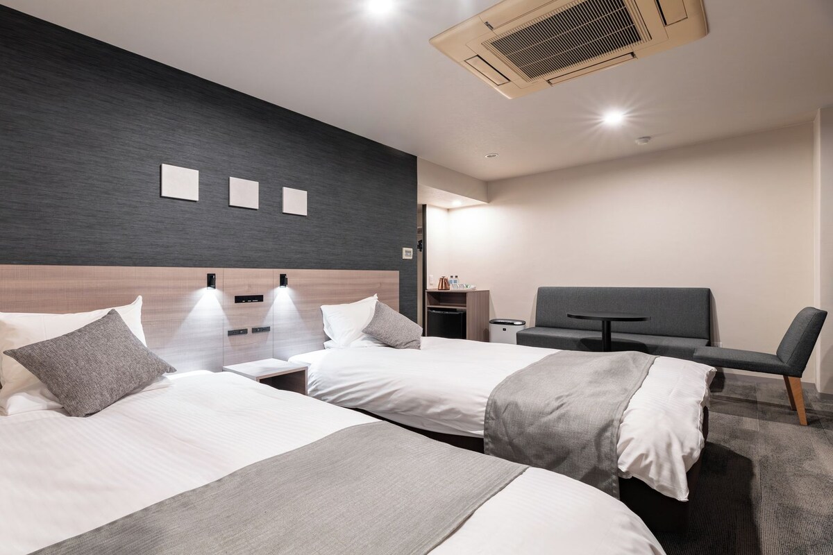 A modern hotel room with two beds, a TV, a desk, and a chair.