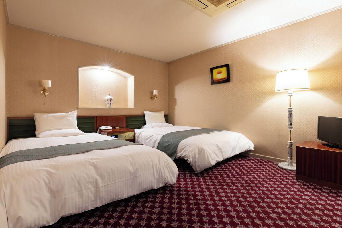 A hotel room with two beds, a nightstand, a lamp, a TV, and a mirror.