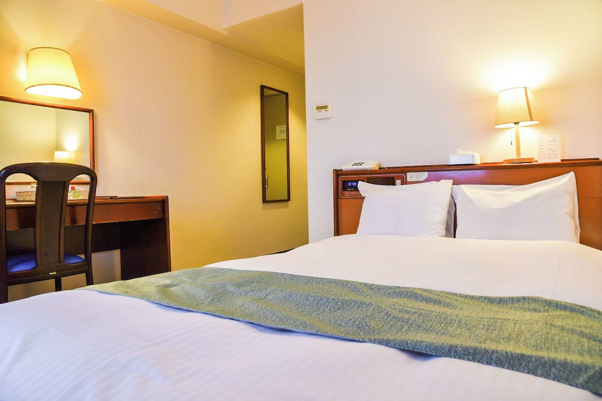 A hotel room with a bed, a desk, a chair, and two wall-mounted lamps.