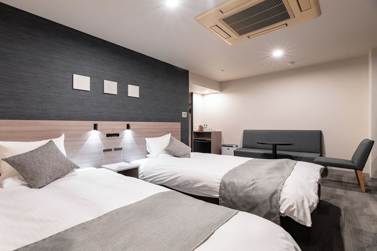 A modern hotel room with two beds, a TV, a desk, and a chair.