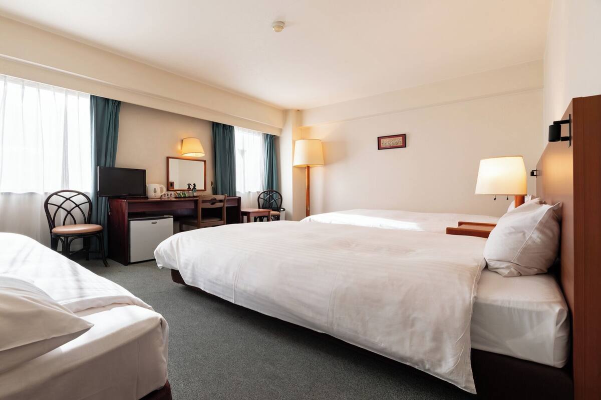 A hotel room with two beds, a desk with a computer, a chair, and two lamps.