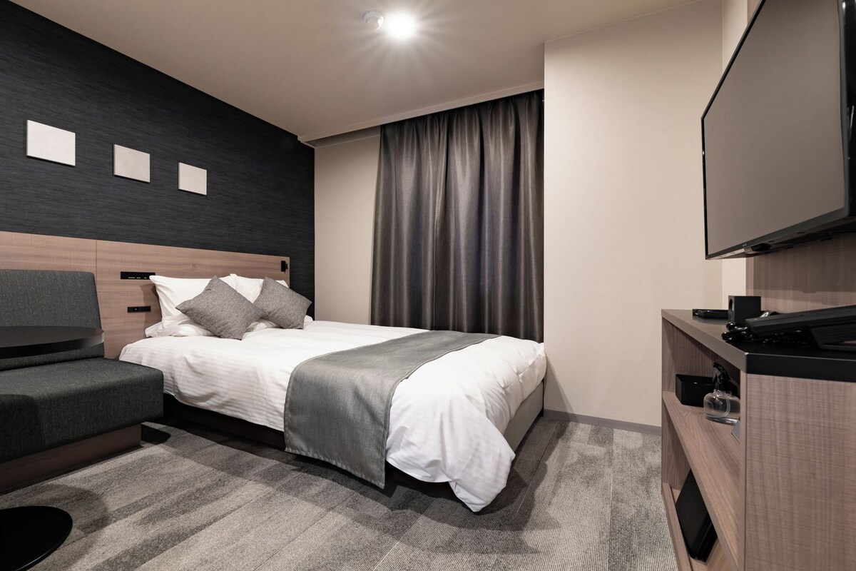 A hotel room with a bed, a desk, a chair, a TV, and a window with curtains.