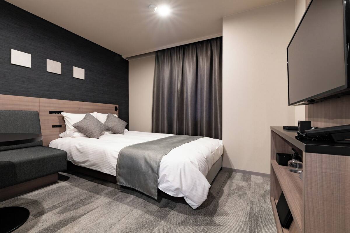 A hotel room with a bed, a desk, a chair, a TV, and a window with curtains.