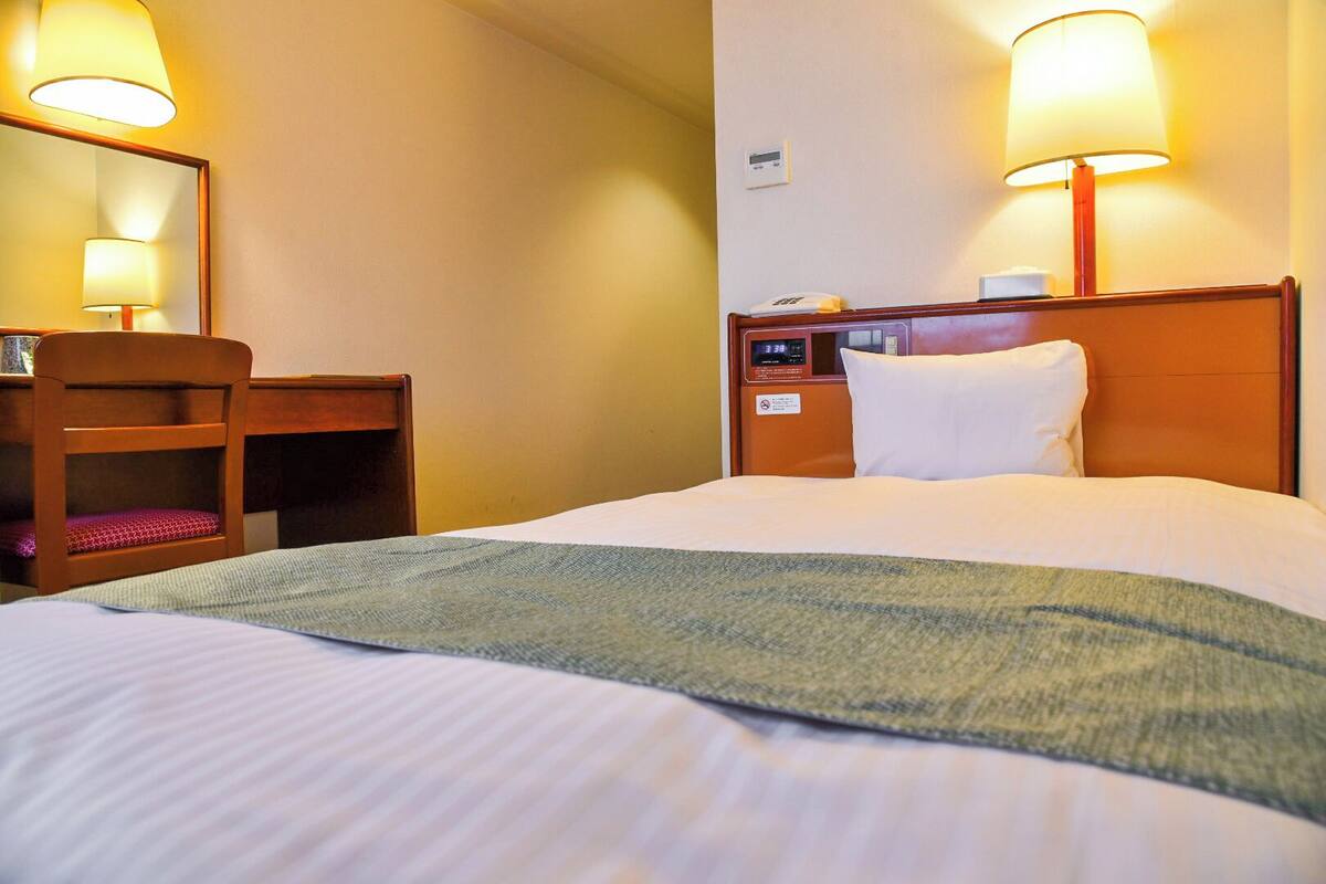 A hotel room with a bed, a desk, a chair, and two bedside lamps.