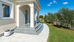 Un bâtiment moderne doté d’une façade en pierre, d’un porche et d’un jardin bien entretenu où l’on peut admirer des oliviers.