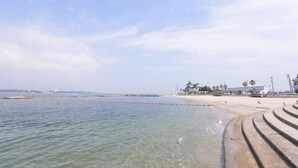 Ein Strand mit klarem Wasser, einem sandigen Ufer und einem Betonweg zum Wasser.