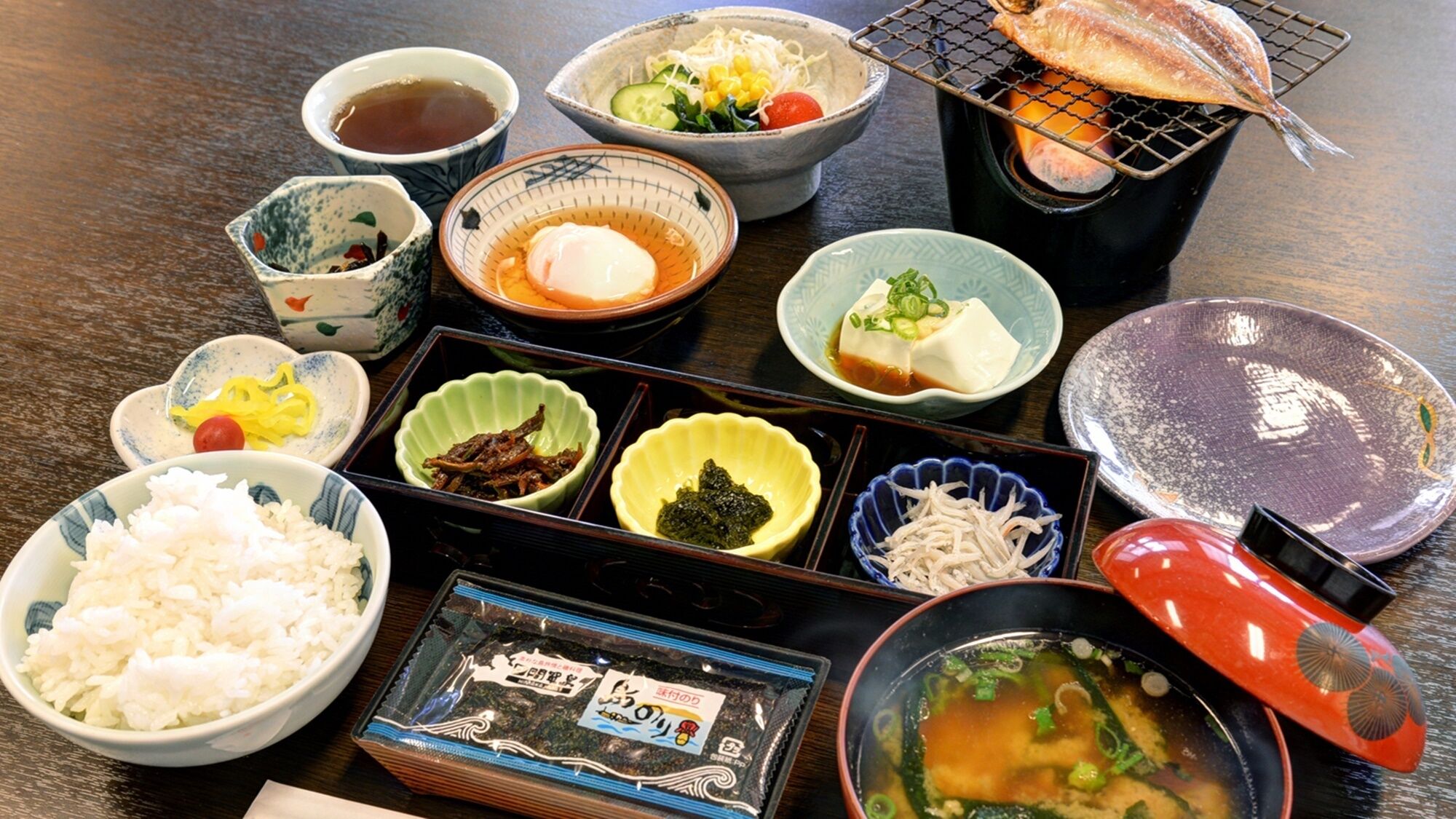 A variety of Japanese dishes including rice, fish, and soup, arranged on a wooden table.