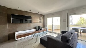Una sala de estar moderna con un sofá seccional grande, un televisor de pantalla plana montado en la pared y una mesa de centro de vidrio.
