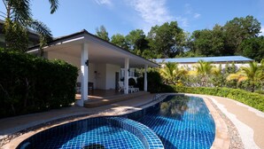 A swimming pool with a curved design, surrounded by a covered patio area and lush greenery. - Yokyor Resort (Sikao)