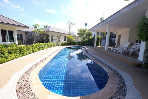 A swimming pool with a tiled edge, surrounded by a pebble border, and adjacent to a covered patio area with lounge chairs. - Yokyor Resort (Sikao)
