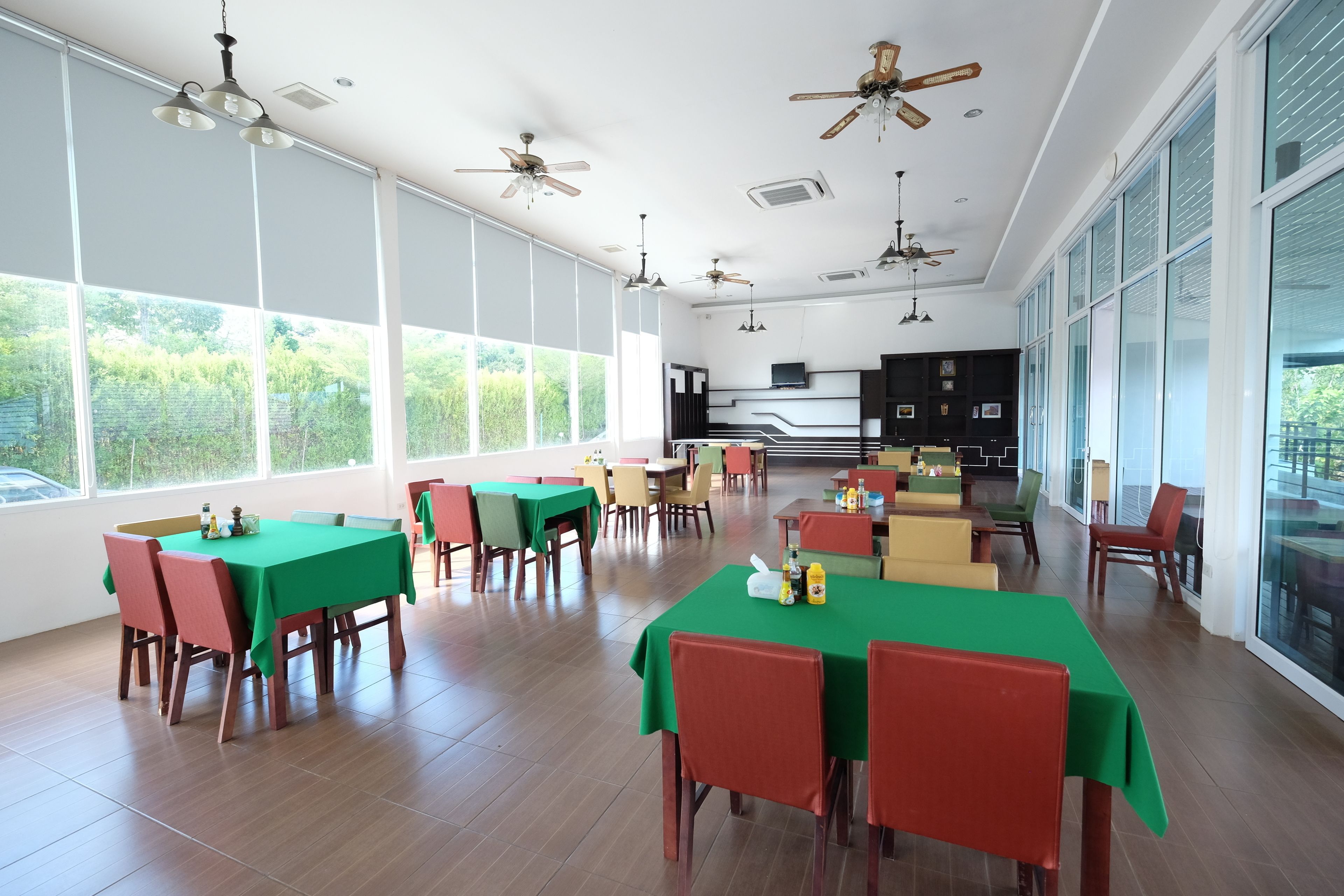 A spacious dining area with multiple tables and chairs, large windows, and ceiling fans.