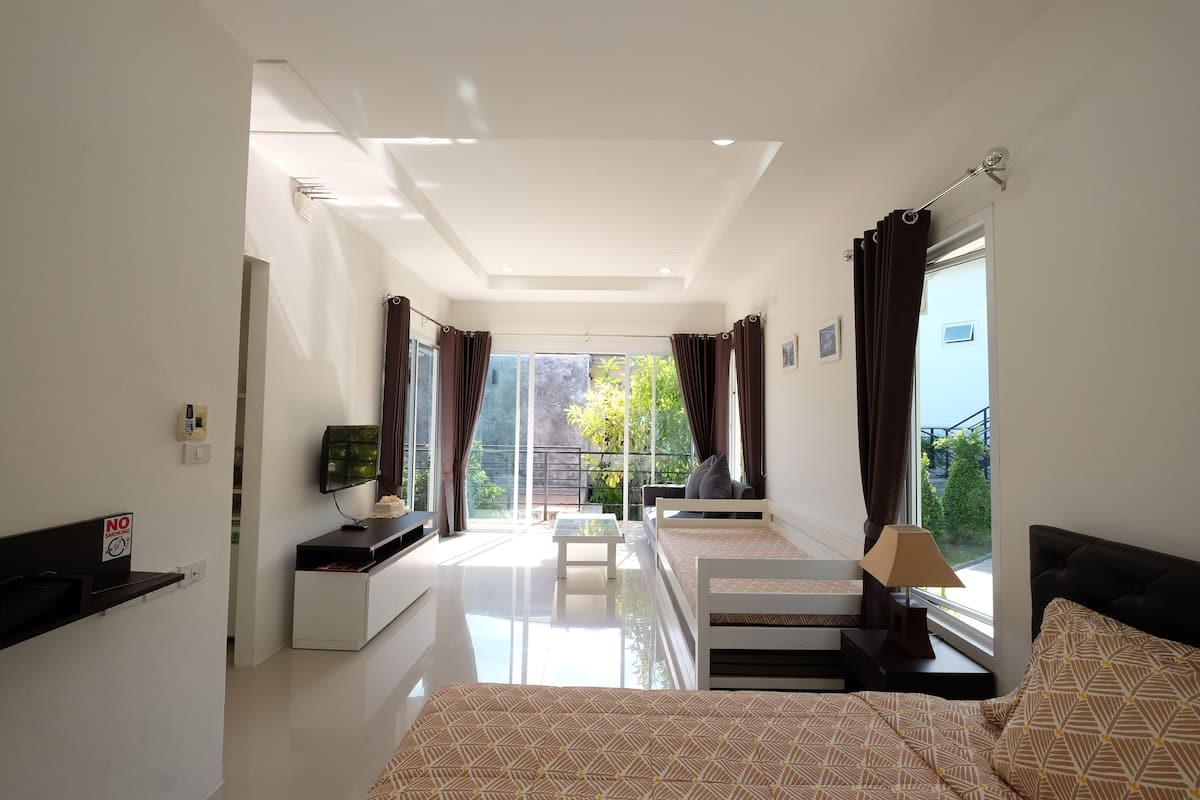 A modern hotel room with a bed, a desk, a TV, and a balcony with curtains.