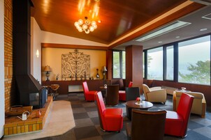 A modern hotel lobby with a checkered floor, red and brown chairs, a large decorative wall piece, and a view through large windows.
