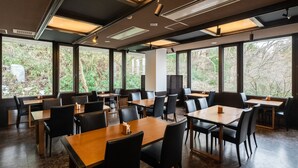 A modern dining area with multiple tables and chairs, large windows offering views of greenery, and recessed ceiling lighting. - Hotel Kasansui (Hakone)