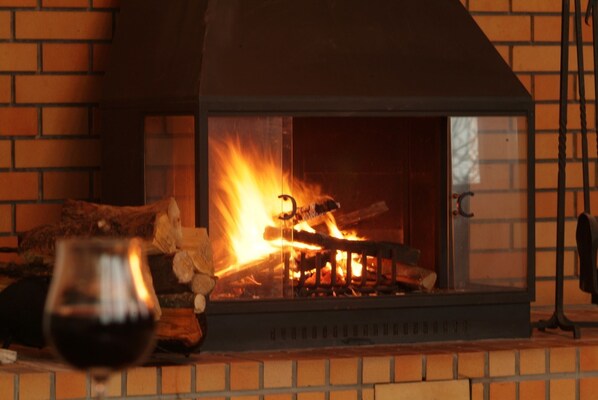 A fireplace with burning logs, a glass of red wine, and a brick wall background.