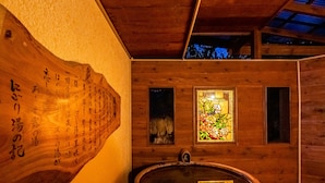 A wooden interior with a wooden bathtub, a wooden wall with calligraphy, and two small windows with floral stained glass. - Hotel Kasansui (Hakone)