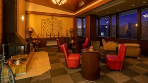 A hotel lobby with a checkered carpet, red chairs, a wooden ceiling, and a large window with a view of the night sky. - Hotel Kasansui (Hakone)