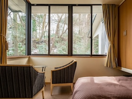 A room with a large window, a bed, a chair, and a desk.