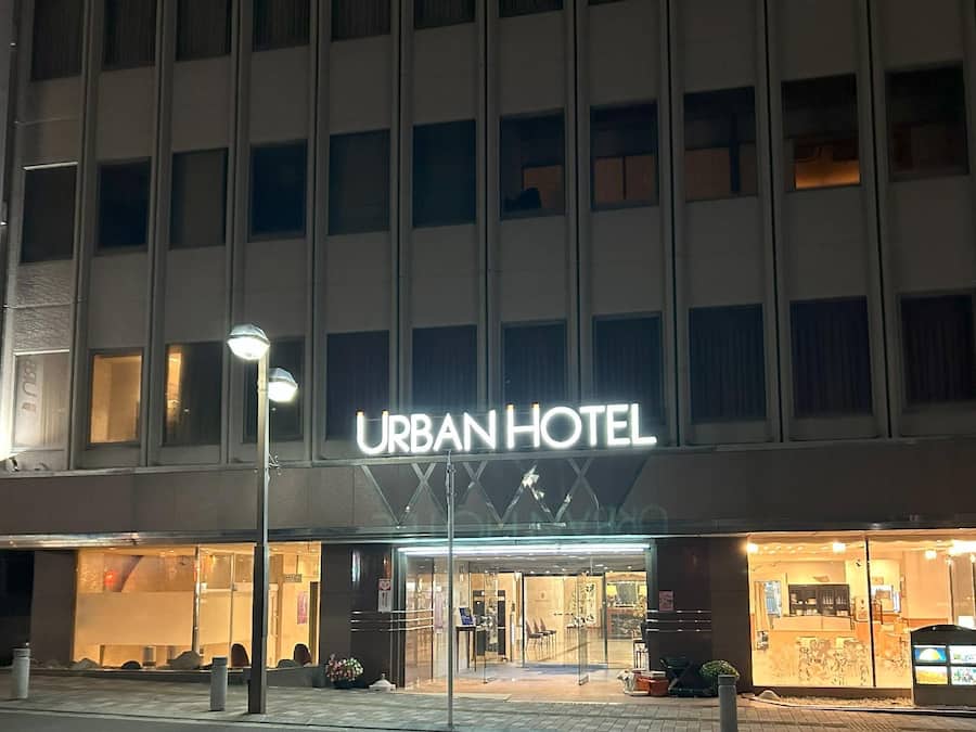 An urban hotel with a prominent sign, a glass entrance, and a visible outdoor seating area.