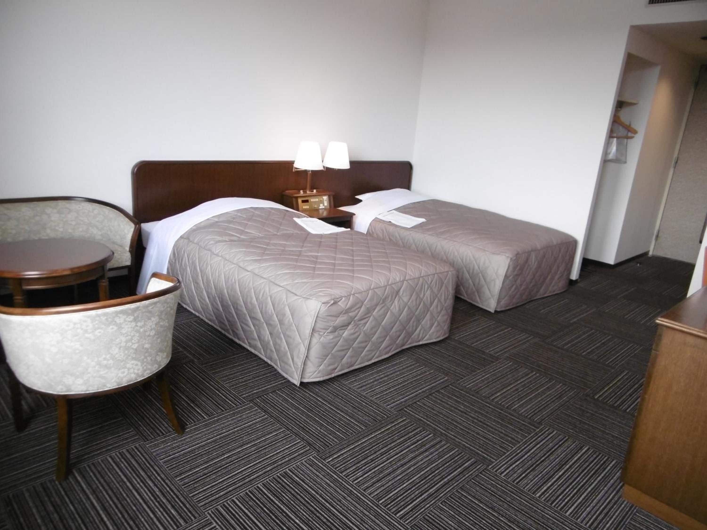 Een hotelkamer met twee bedden, een stoel, een klein tafeltje en een nachtkastje met lampen.