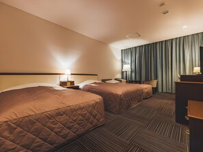 Habitación de hotel con dos camas, un escritorio, una silla y un amplio ventanal con cortinas.