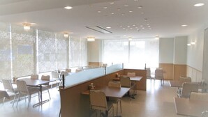 A spacious conference room with a long table and chairs, large windows with sheer curtains, and recessed ceiling lighting.