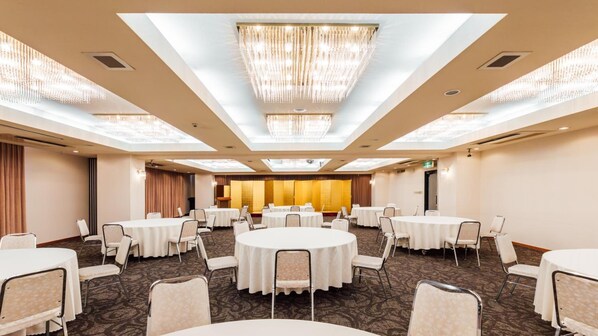 Une salle de conférence d’hôtel avec des tables rondes, des chaises et un lustre.