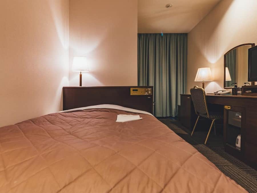 Una camera d'albergo con un letto, una scrivania con una sedia, una televisione e una finestra con tende.