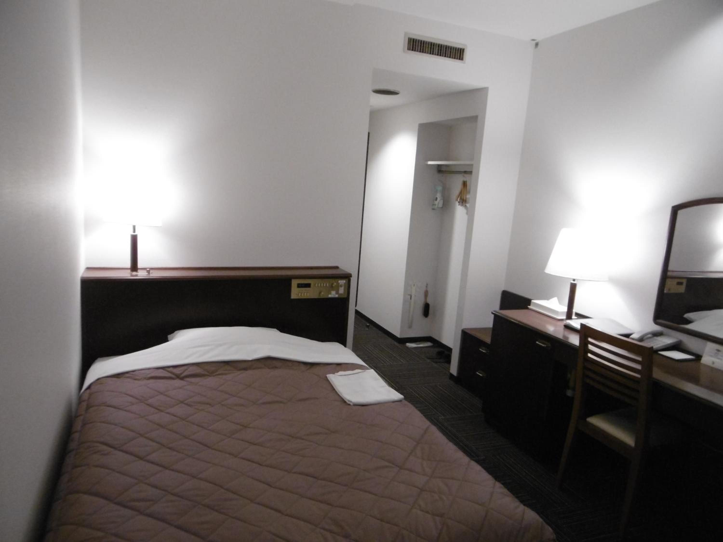 A hotel room with a bed, a desk, a chair, a mirror, and a wardrobe.
