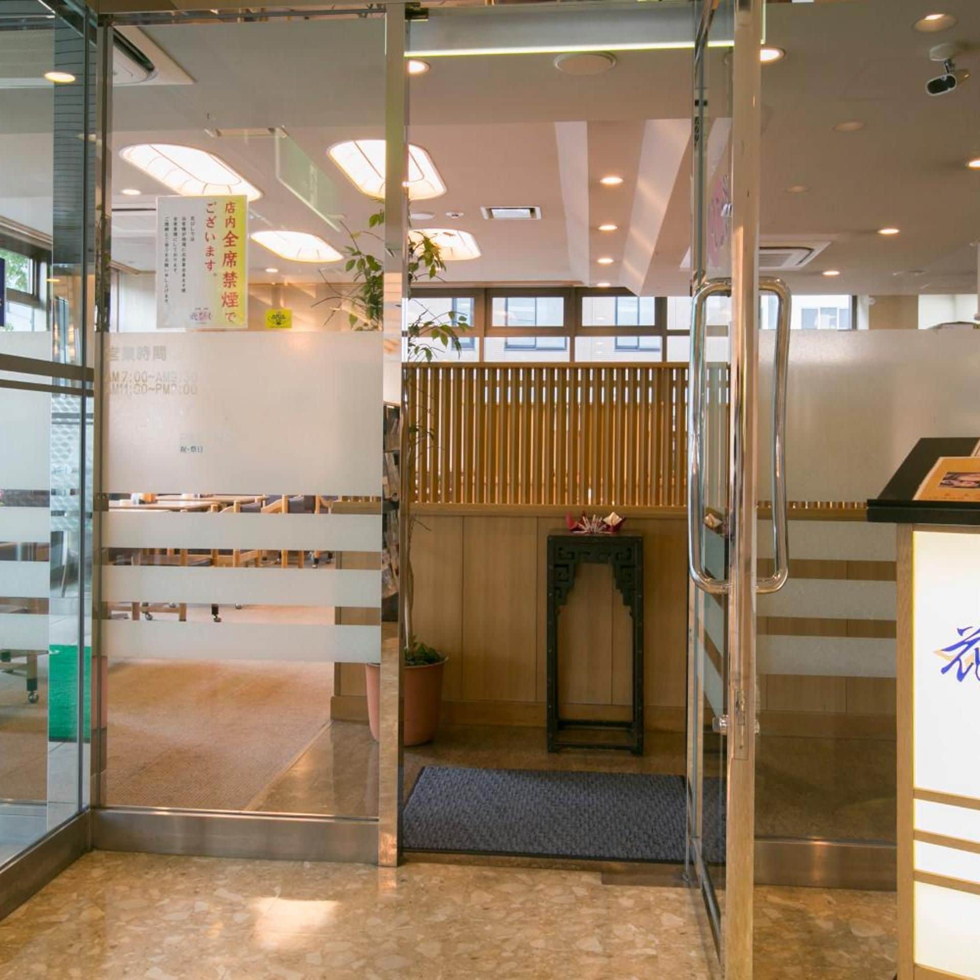 A hotel reception area with a glass door, a reception desk, a seating area with benches, and a wooden partition.