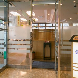 A hotel reception area with a glass door, a reception desk, a seating area with benches, and a wooden partition. - Yokkaichi City Hotel Annex (Yokkaichi)