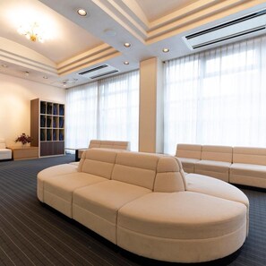 A modern living room with a sectional sofa, a built-in wardrobe, and a large window with sheer curtains. - Yokkaichi City Hotel Annex (Yokkaichi)
