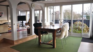 A spacious living area with a wooden dining table, white chairs, and a green rug. There is a television and a sofa in the background. - Lovely home in Otterup with WiFi (Otterup)