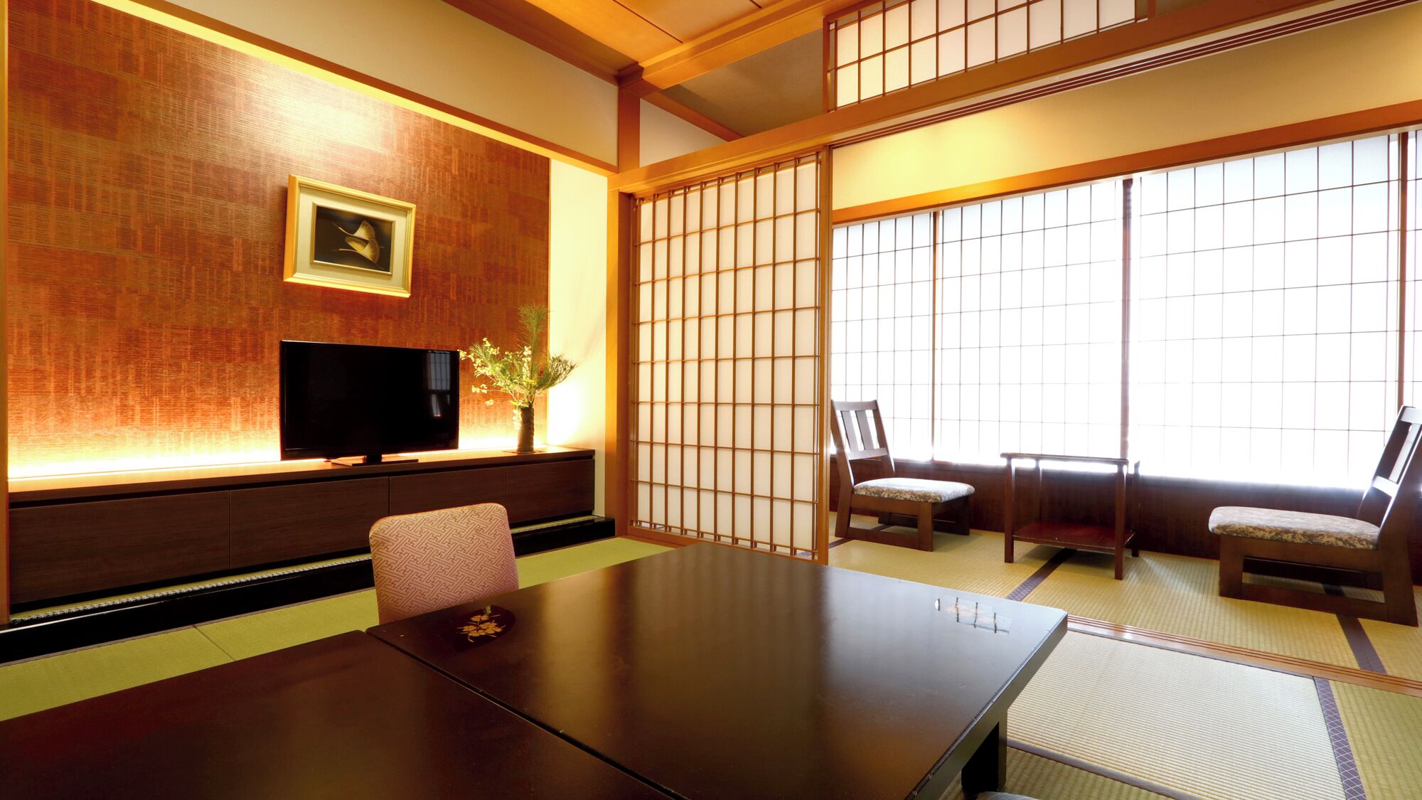 Ett traditionellt japanskt rum med tatamimattor på golvet, ett lågt bord, två stolar, en tv och en shojiskärm.