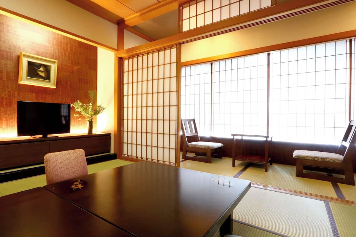 A traditional Japanese room with tatami flooring, a low table, two chairs, a television, and a shoji screen.