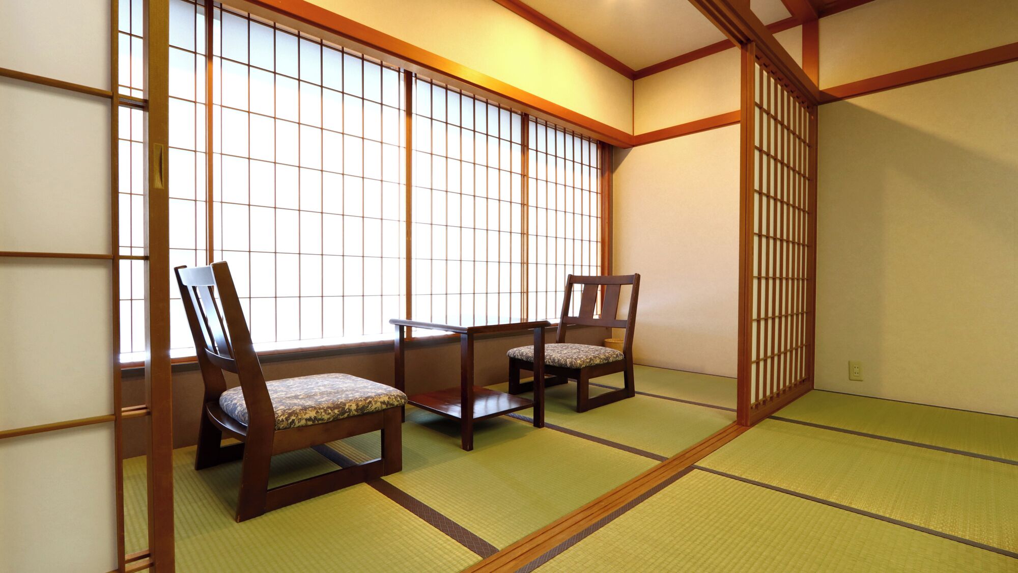Ett traditionellt japanskt rum med tatamimattor på golvet, shojiskärmar och två trästolar.